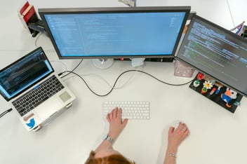 Student med tre PC-er til bruk ved IT-utdanning på nett.